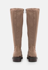 Une paire de bottes en suède marron hautes avec des fermetures éclair à l'arrière et des talons bas empilés, vues de derrière sur fond blanc.