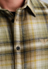 Camicia di flanella a quadri verde e beige con bottoni neri e logo ricamato sul petto. Tessuto morbido e colletto strutturato.