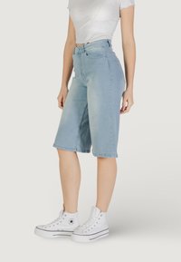 Bermuda shorts in denim azzurro chiaro con vita alta, chiusura frontale con bottone e tasche laterali, abbinati a sneakers alte bianche.