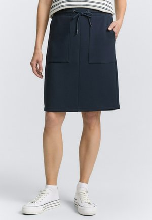 Navy blue knee-length skirt made of stretchy fabric, features two front pockets and an adjustable drawstring waist. Paired with white sneakers.