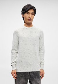 Απαλό γκρι πλεχτό πουλόβε�ρ με σπογγώδη υφή, στρογγυλή λαιμόκοψη και ραμμένες μανσέτες. Συνδυάζεται με σκούρες γκρι τζιν, παρουσιάζοντας μια casual εμφάνιση.