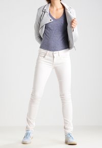 Grå zip-up jacka över en blå t-shirt, ihop med vita skinny jeans och ljusblå sneakers. Kännetecken inkluderar en figurnära design och slät textur.