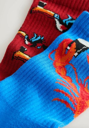 Vícebarevné podkolenky: jedny červené s výraznými motivy tukanů, druhé modré s jasným grafickým motivem humra. Měkká pletená textura.