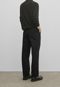 Pantaloni neri realizzati in un tessuto testurizzato, con una vestibilità ampia e gamba dritta. Abbinati a una maglietta a maniche lunghe scura e scarpe nere.