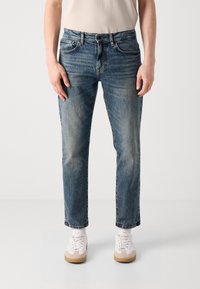 Blugi din denim de culoare albastru deschis cu o croială dreaptă, având talie medie, ușoare decolorări, cinci buzunare și un închidere clasică cu buton și fermoar.