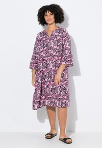 Rosa Leopardenmusterkleid mit V-Ausschnitt, dreiviertellangen Glockenärmel und lockerer Passform. Kombiniert mit schwarzen Slipper-Sandalen.