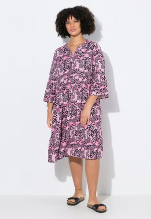 Vestido de leopardo rosa con escote en V, mangas de tres cuartos acampanadas y corte relajado. Combinado con sandalias negras tipo deslizante.