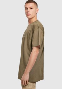 Olivengrøn bomulds t-shirt med afslappet pasform, korte ærmer og rund halsudskæring. Har enkle tekstdetaljer på forsiden.