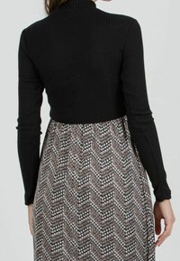 Haut noir à manches longues côtelé associé à une jupe à motifs avec un design en chevrons, des points blancs et des accents terreux.