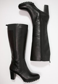 Botas negras hasta la rodilla hechas de cuero suave, con un tacón ancho, suela texturizada, cremallera lateral y panel elástico para un ajuste cómodo.