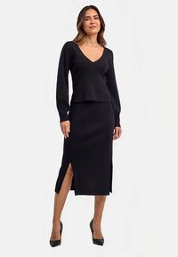Completo nero in maglia a due pezzi composto da un top a maniche lunghe con scollo a V e una gonna midi abbinata con spacchi laterali. Texture liscia e design aderente.