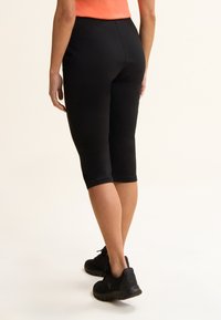 Leggings capri negros con textura lisa y diseño ajustado, que terminan justo debajo de la pantorrilla. Combinados con zapatillas negras.
