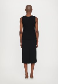 Schwarzes ärmelloses Oberteil mit gewelltem Ausschnitt, kombiniert mit einem knielangen schwarzen Rock. Glatter Stoff und schlichte Silhouette.