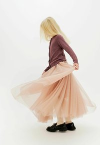 Cárdigan lila claro combinado con una falda de tul en tono rosa empolvado, fluida y de capas, que presenta lunares. Unos zapatos de charol negros completan el look.