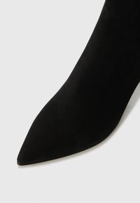 Chaussure à talon aiguille en suédé noir avec un bout pointu et une texture lisse. Le design présente un talon mince et une silhouette élégante.