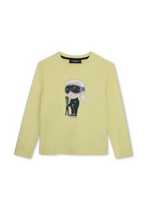 Chemise à manches longues jaune clair avec un dessin animé d'une personne portant des lunettes de ski et tenant des skis au centre devant.