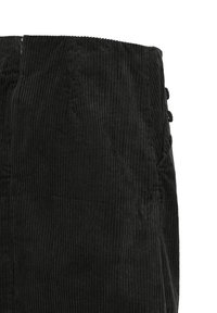 Tissu en velours côtelé noir avec des côtes verticales et des boutons latéraux, montrant la texture et un détail partiel du vêtement sur fond blanc.