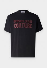 T-shirt in cotone nero con testo rosso in rilievo "VERSACE JEANS COUTURE" in carattere audace. Design a maniche corte e collo rotondo.