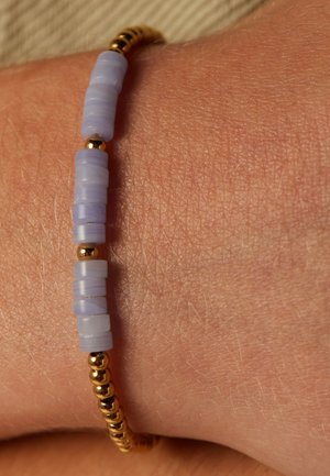 Paarse cilindrische kralen en gouden ronde kralen vormen een armband die op de huid wordt gedragen, met een gladde textuur en afwisselende kleuren.