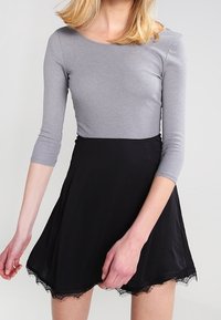 Šedý top s dlouhým rukávem spárovaný s černou sukní. Sukně má rozšířený design a krajkový lem, což vytváří kontrastní texturu.