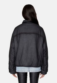 Czarna puchowa kurtka o fakturowanym wykończeniu, z wysokim kołnierzem i pikowaniem na ramionach. Nosi się ją na jasną koszulę dżinsową.