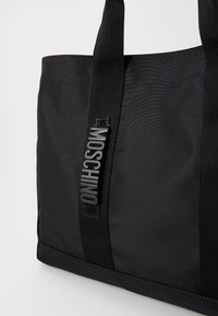 Czarna torba tote z nylonu, charakteryzująca się mocnym materiałem, podwójnymi uchwytami oraz wypukłym znakiem logo "MOSCHINO" z boku. Gładka tekstura i strukturalny design.