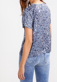 Top corto de estampado de leopardo azul en tejido ligero, con cuello redondo y un ajuste relajado, combinado con jeans de color azul claro.