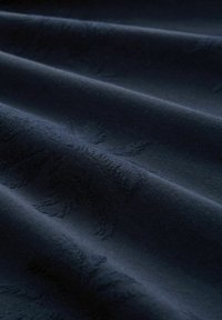 Donker marineblauwe stof met een subtiele geperste bladmotief. Het materiaal heeft een gladde textuur en valt in zachte plooien.