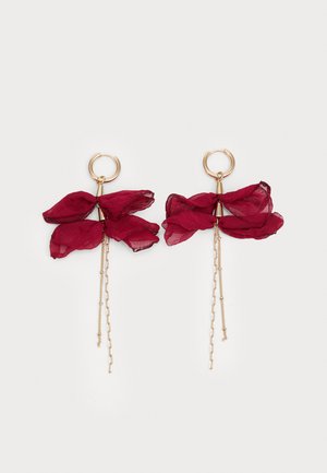 Boucles d'oreilles en or en forme de cercle avec des pétales en tissu transparent bordeaux superposés et des chaînettes dorées délicates sur fond blanc.