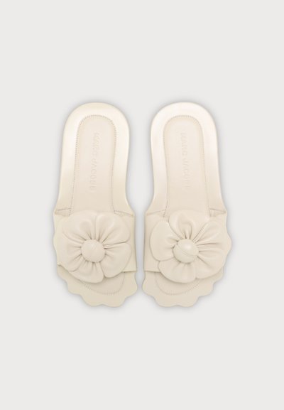 Sandales plates couleur crème avec bords festonnés et grandes fleurs en tissu souple sur les brides, vues de dessus.