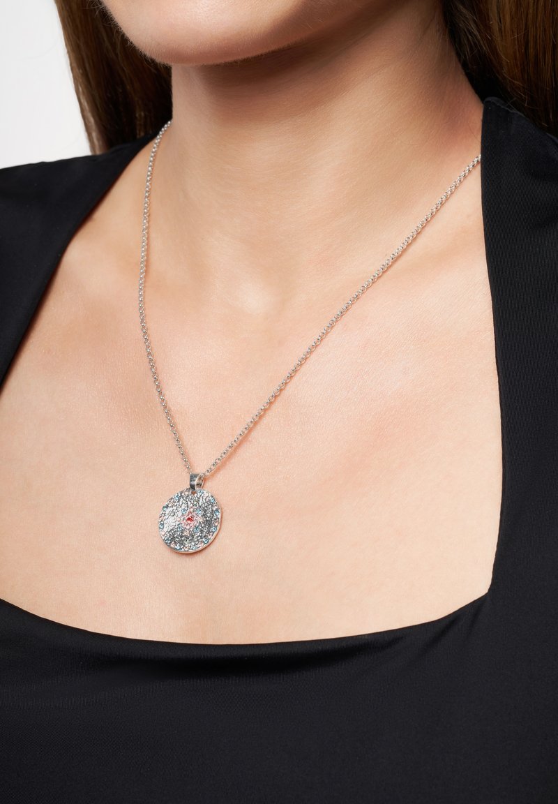 Söljd halsband med en rund anhängare som har en texturerad yta och en central röd accent. Tillsammans med en delikat kedja.