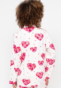 Langdurige pyjama's met lange mouwen in witte stof, met een patroon van roze harten en kleine rode accenten. Zachte textuur met een losse pasvorm.