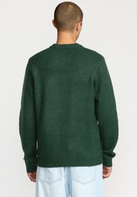 Pull vert en maille avec un col rond côtelé, des manches longues et une coupe légèrement oversize. Texture douce et design décontracté.