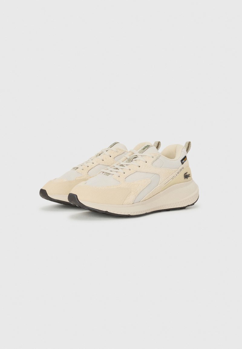 Le scarpe da ginnastica beige presentano un upper in materiali misti con accenti in suede e mesh. La suola è di colore crema con un battistrada nero. Logo Lacoste sul lato.
