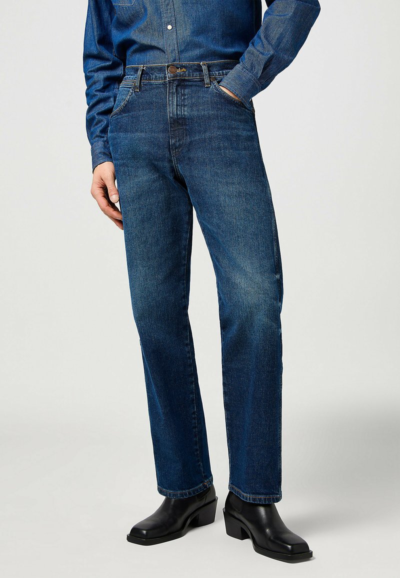 Jeans in denim blu scuro con taglio dritto, design a cinque tasche e leggera scoloritura. Indossati con stivaletti neri alla caviglia.
