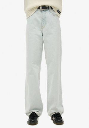 Jasnoniebieskie dżinsy z szerokimi nogawkami i wysokim stanem, czarny pasek oraz czarne mokasyny, noszone z kremowym swetrem wpuszczonym do środka.