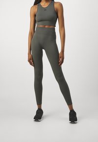 Olivově zelený sportovní crop top s designem racerback, kombinovaný s legínami vysokého pasu ve stejné barvě, které mají hladkou texturu.