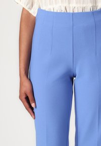 Tailored blue trousers made from smooth fabric feature a high waist, sharp creases, and a fitted silhouette, accentuating the form.