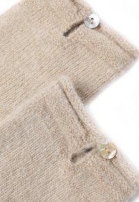 Beige gebreide stof met een gestructureerde afwerking, voorzien van lichte metalen draden en twee ronde, iriserende knopen bovenaan.