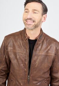 Bruine leren jas met een gestructureerde afwerking, rits aan de voorkant en geribbelde kraag. Voorzien van horizontale stiksels en knoopaccenten.