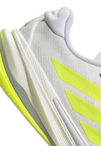 White athletic shoe with bright yellow stripes and accents, textured fabric, and a thick, multi-layered sole.
