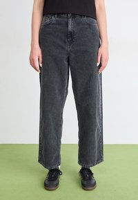 Široké čierne džínsy vyrobené z denimu, s vyblednutým vzhľadom, prednými vreckami a vysokým pásom. Skombinované s čiernymi šnurovacími topánkami.