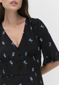 Schwarzes Blumenkleid mit blauen Blumenmustern, kurzen Rüschensäumen, einem tiefen V-Ausschnitt und dekorativen Knöpfen vorne.