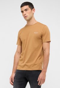 T-shirt à manches courtes, col rond, de couleur marron clair, en tissu doux, avec un petit logo de marque blanc sur la poitrine.