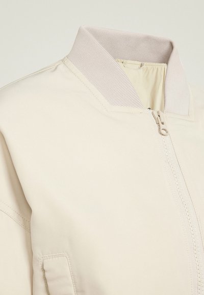 Lichtbeige bomberjack met een geribde kraag, voorrits en een gladde stof met stikdetails. Geen zichtbare patronen of hardware.