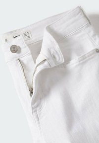 Pantalones vaqueros blancos de mezclilla con cremallera plateada, cierre de botón metálico y una etiqueta con información de talla. La tela parece suave y resistente.