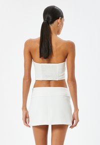 Valkoinen olkaimeton crop-top, jossa on smockattu yksityiskohta selkäpuolella, yhdistettynä valkoiseen minihameseen, joka on sileä ja jossa on litteä vyötärö.