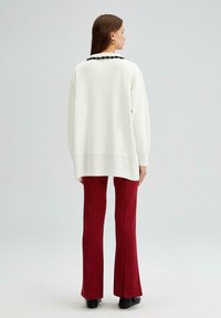 Oversized wit sweater met ribbelzoom, voorzien van een zwarte gegolfde rand. Gecombineerd met aansluitende, lange rode broeken en zwarte enkellaarsjes.
