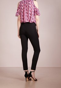 Top floreale con spalle scoperte e maniche a volant, abbinato a pantaloni neri slim-fit e sandali neri con tacco alto e dettaglio a fiocco.
