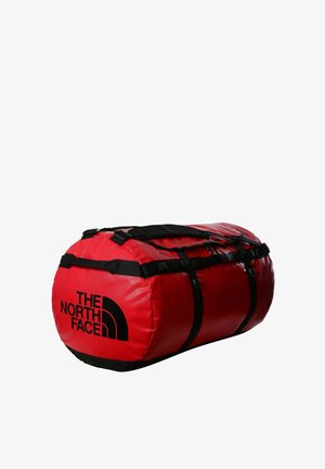 Bolsa de deporte roja con asas y acentos negros. Tiene una forma redonda y un logotipo negro prominente. Está hecha de material duradero.